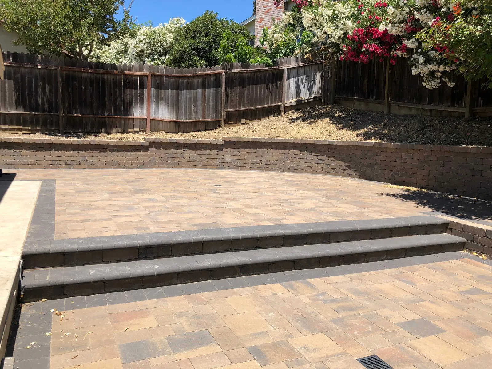 Outdoor patio with paver stones, steps, and a retaining wall, crafted by an expert paving installer. Trees with flowers and greenery create a lush backdrop, perfect for relaxing or entertaining in your Bay Area home.