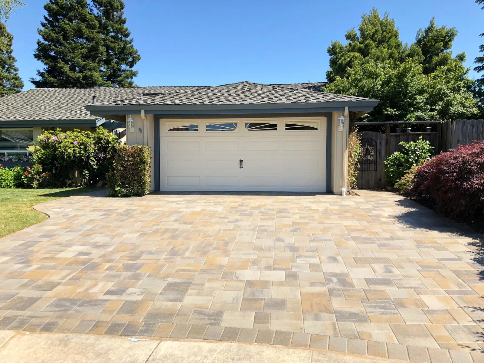 A house with a white double garage and a driveway featuring interlocking paving in tan and gray, expertly installed by a leading paving installer in the Bay Area.