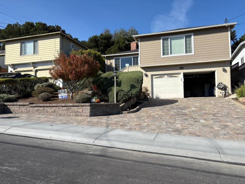 Two-story tan house with a single garage, landscaped front yard, and a driveway expertly finished by a bay area paver contractor on a sunny day.