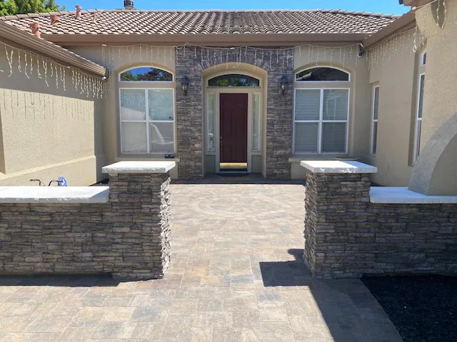 Front patio of a house with stone walls, tiled floor by a skilled paving installer, two windows, and a red front door—perfect for Bay Area living.