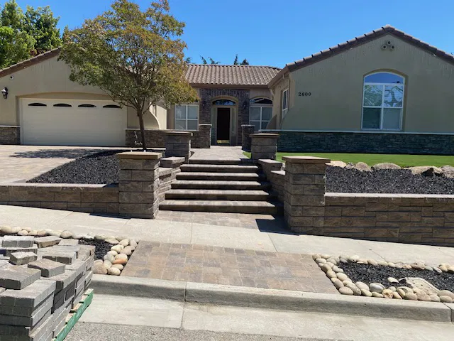 Single-story house with stone steps, a tree, and a landscaped front yard featuring rocks and expert paver contractor-installed pavers.