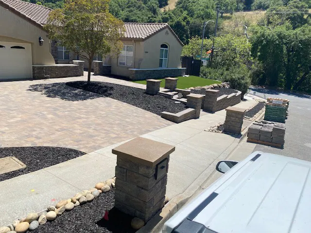 A suburban Bay Area home with a paver stone driveway, stone pillars, and a landscaped front yard along a curved sidewalk.