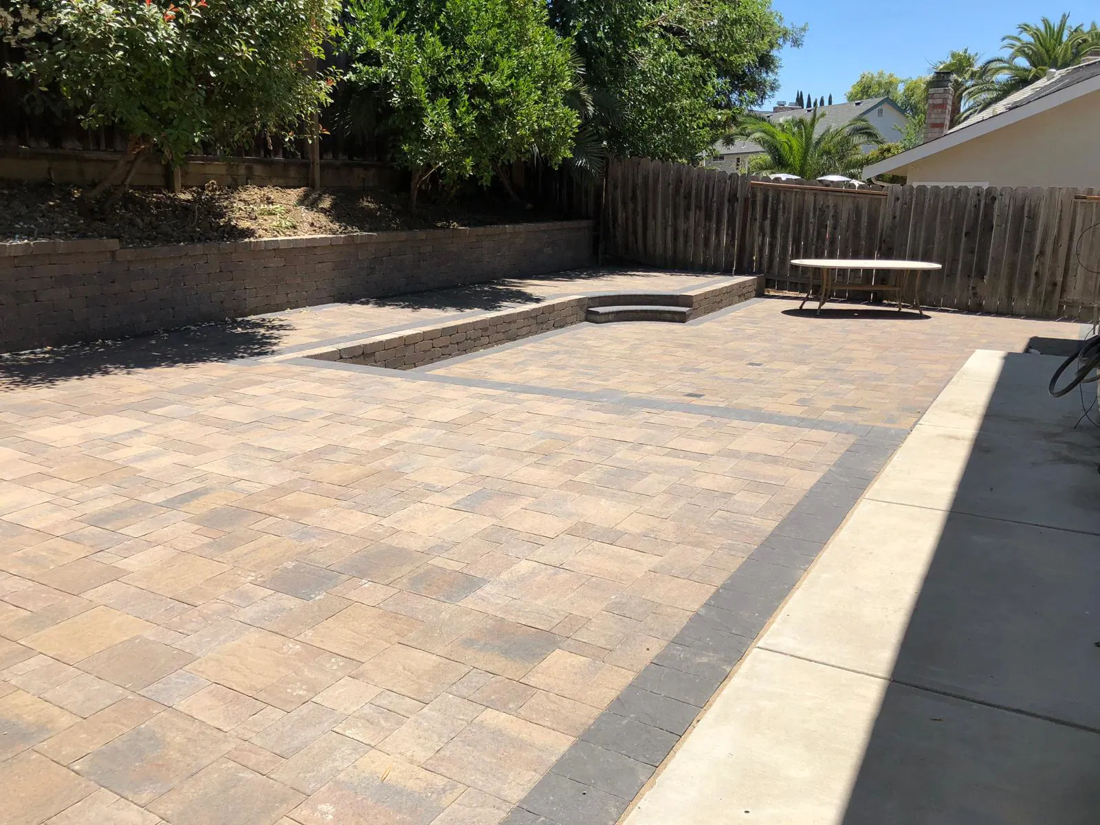Spacious backyard patio with stone pavers installed by a paving bay area expert, featuring a picnic table, steps, trees, and a wooden fence.
