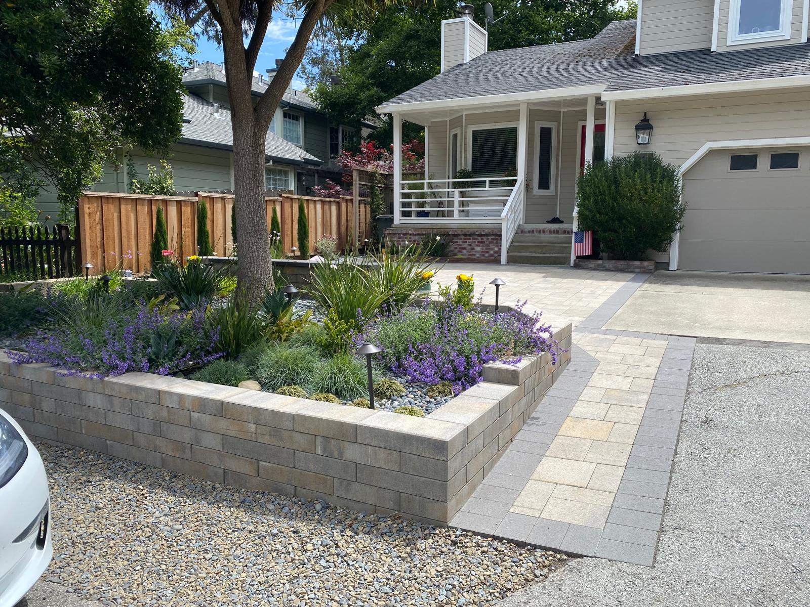 Front yard with a raised flower bed, stone wall, interlocking paving walkway, and a house with a porch in the background—perfect for classic Bay Area curb appeal.