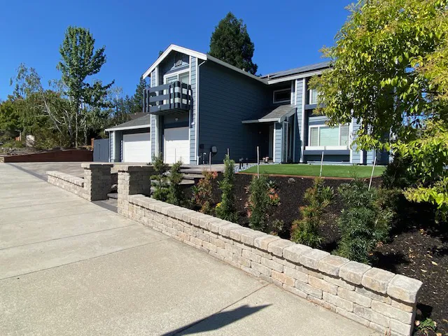 Modern two-story house with dark blue siding, white trim, a stone retaining wall along the driveway, and elegant interlocking paving installed by a skilled paving installer in the Bay Area.