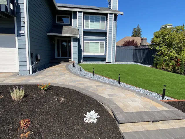 Modern gray house with a landscaped yard, paver stone walkway, green lawn, and mulch garden bed in the Bay Area.